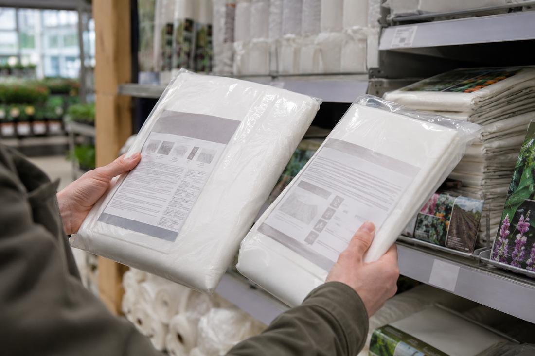 Twee verpakkingen vliesdoek vergelijken in een tuinwinkel
